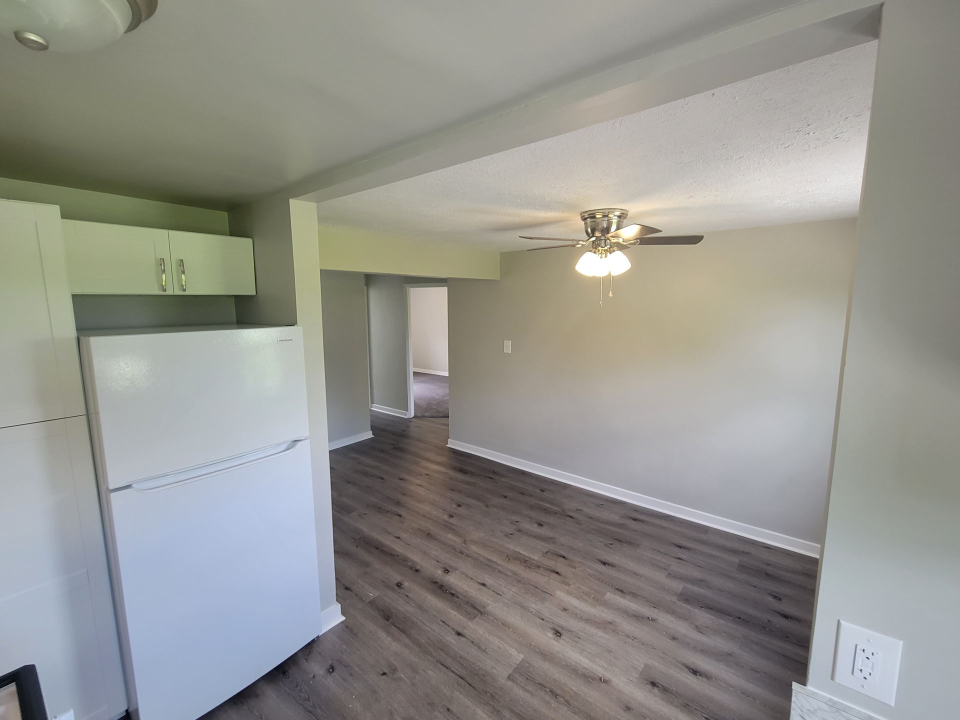 A living room with hardwood floors , a refrigerator and a ceiling fan.