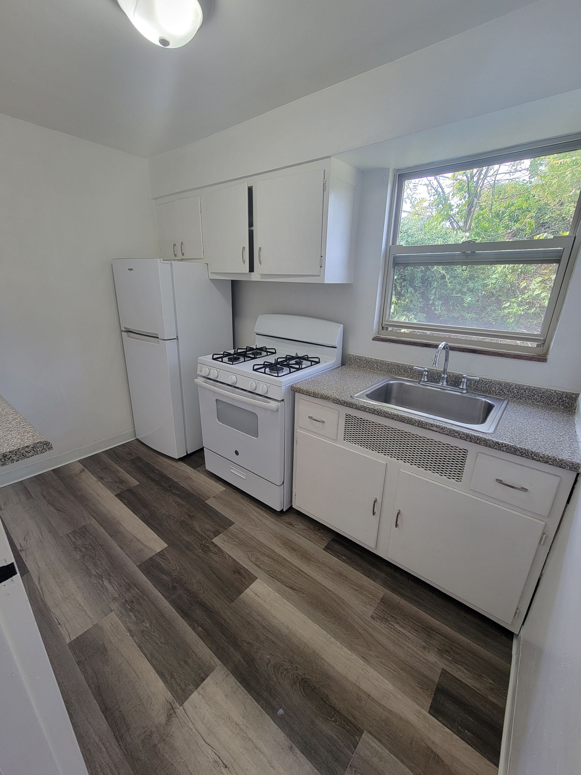 A kitchen with a stove , refrigerator , sink and window.