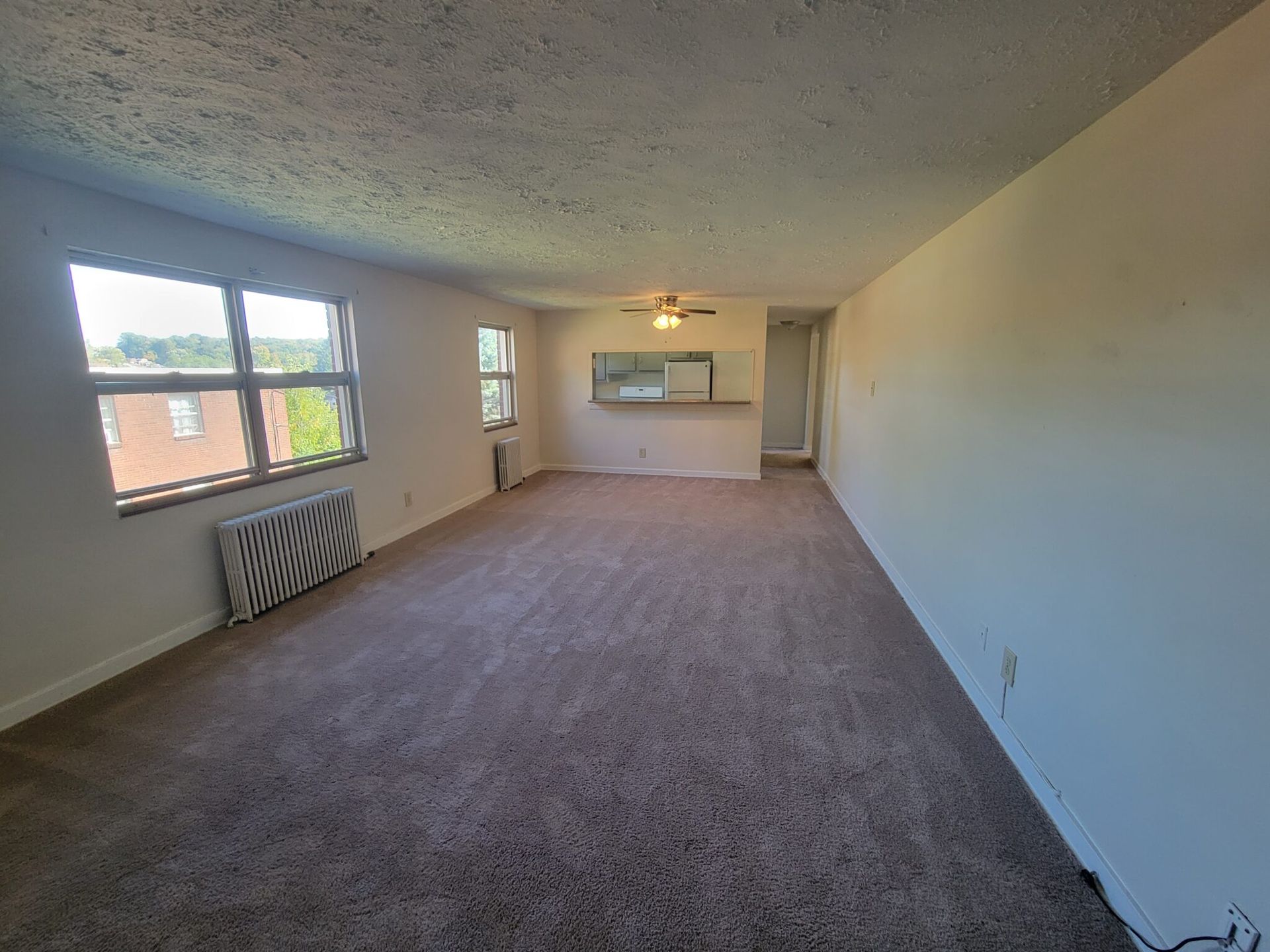 An empty living room with a ceiling fan and a window.