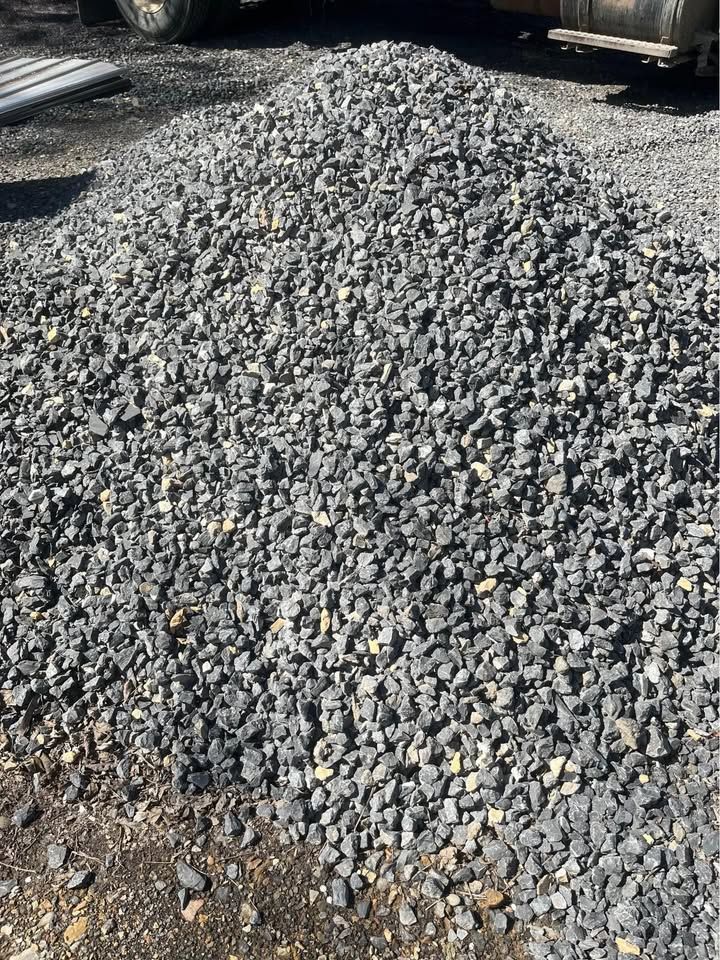 Pile of gray gravel on a dark surface, possibly a construction site.
