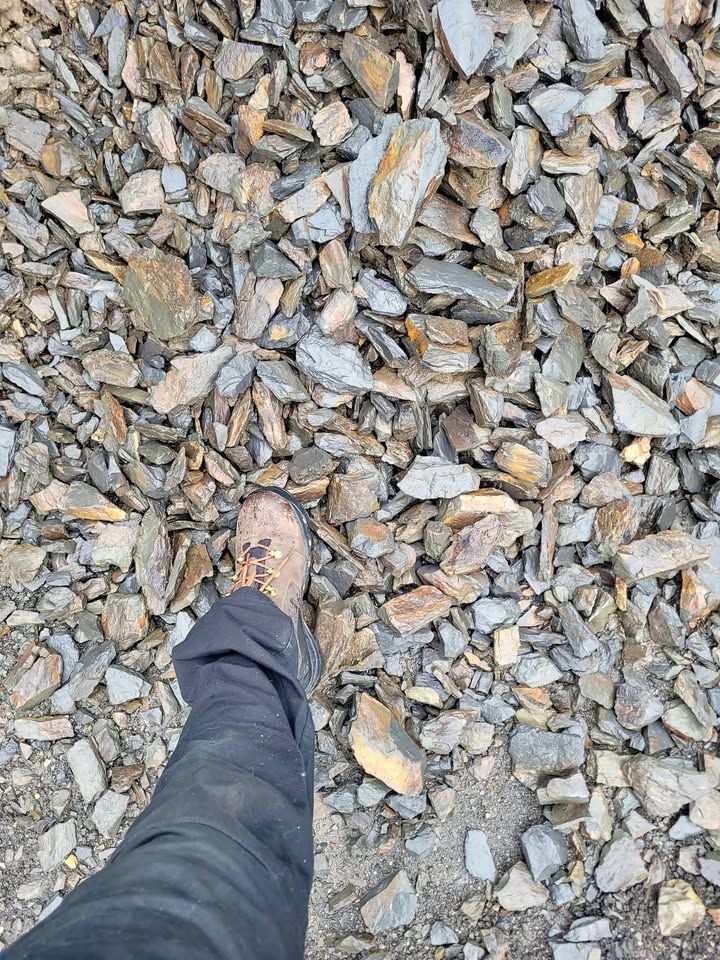 Foot stepping on a surface of slate-like stones, tan boot, dark pants, outdoor setting.