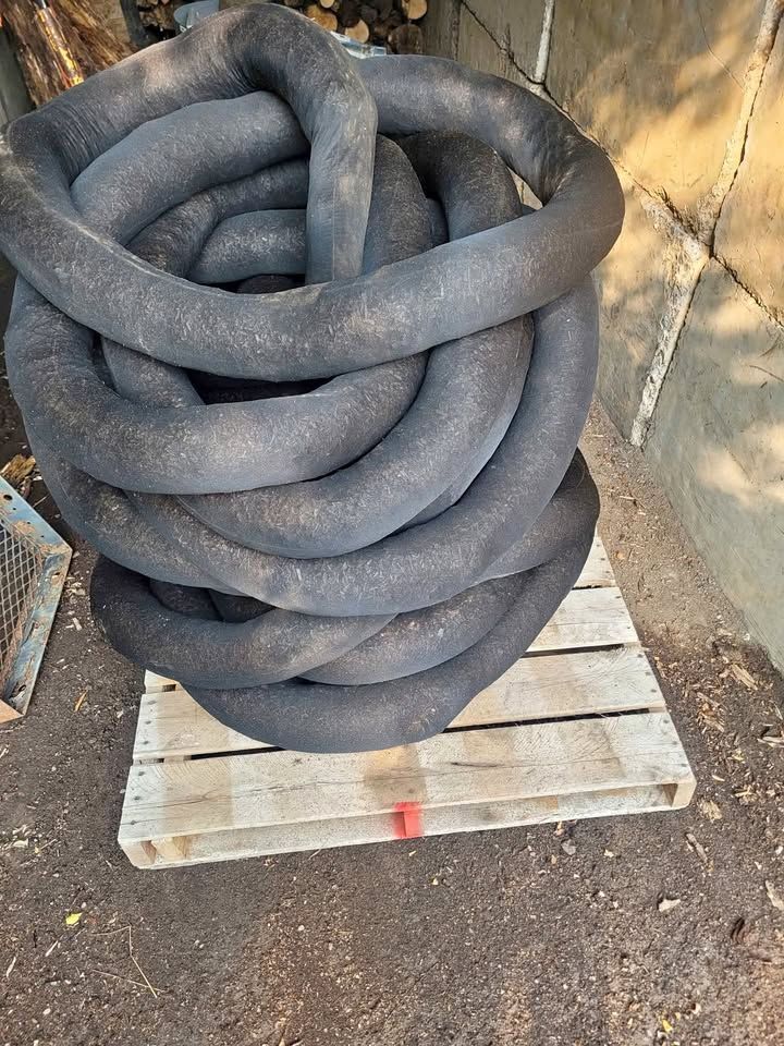 Coiled, dark gray oil absorbent booms stacked on a wooden pallet outdoors.