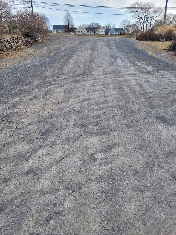 Gravel road leading uphill toward several houses on a sunny day.