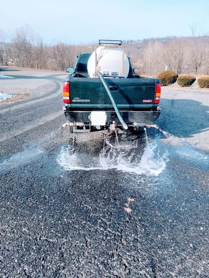 Truck spraying water on asphalt pavement. White tank in the bed. Clear, sunny day.