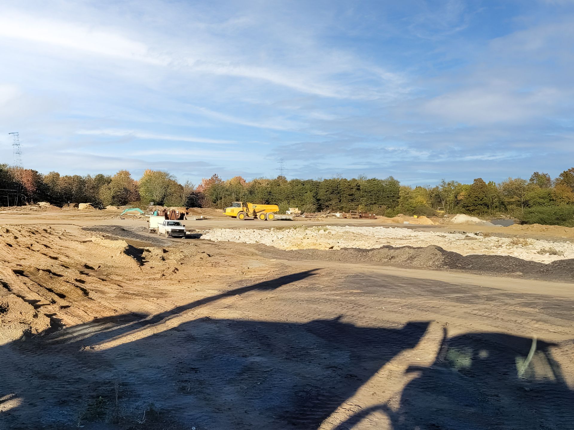 Construction site with earth-moving equipment and piles of dirt under a partly cloudy sky.