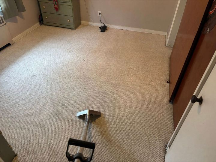 Carpeted room with a vacuum cleaner on the floor and a dresser in the corner