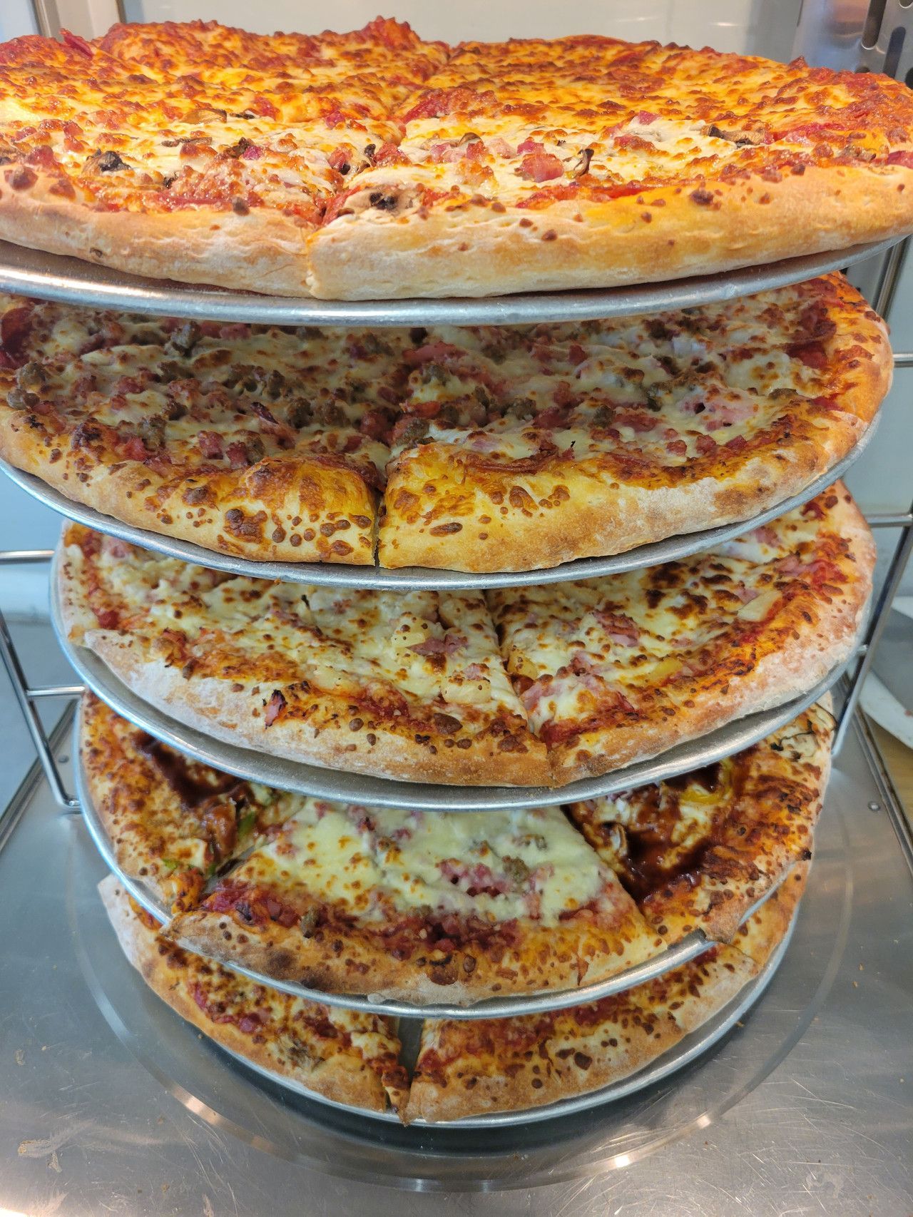 Four pizzas stacked on a metal rack, with a variety of toppings and visible crusts.