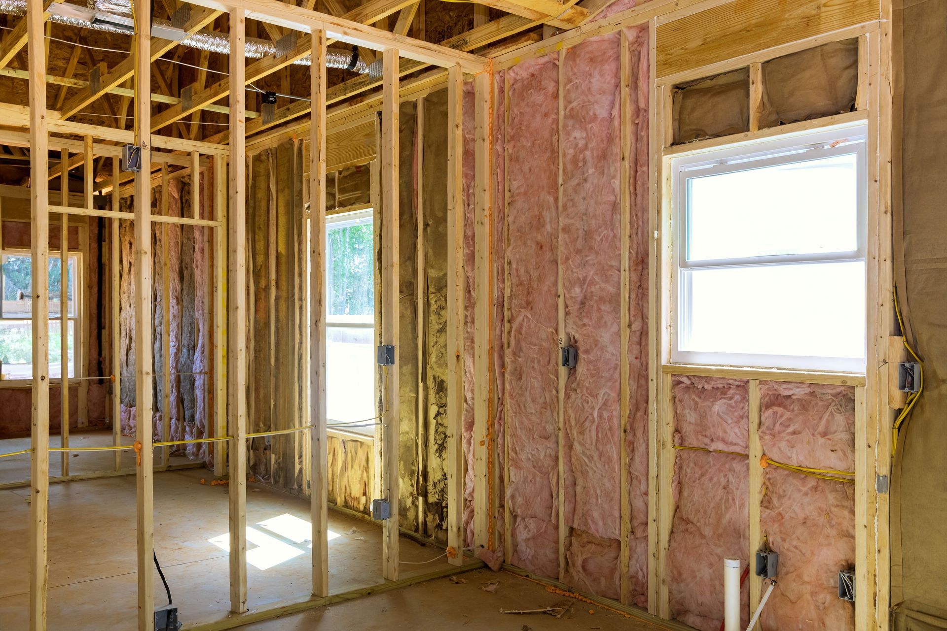 Interior of a house under construction, showing wooden framing, insulation, and windows.