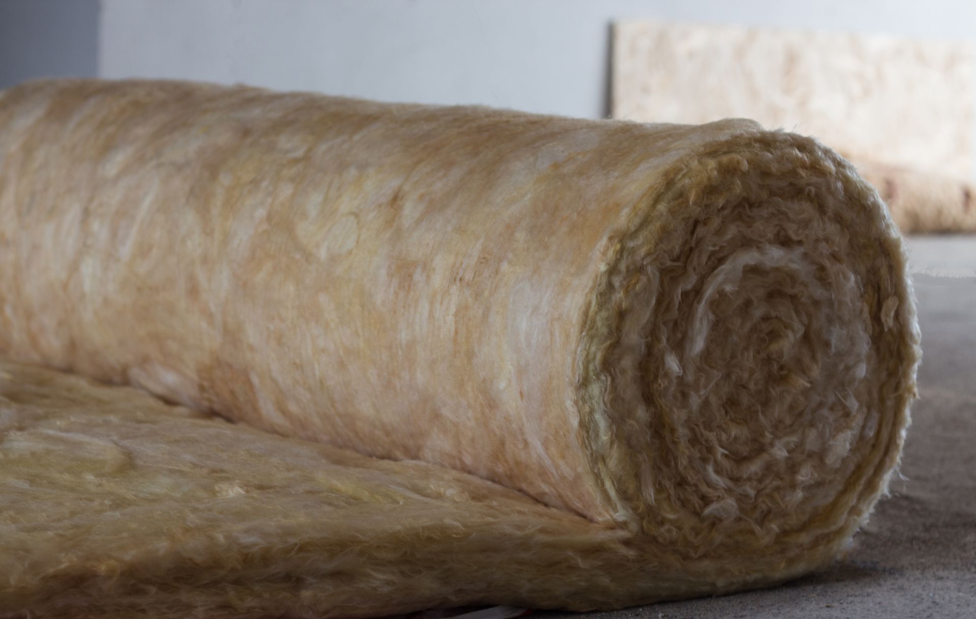 Roll of tan fiberglass insulation on a gray surface.