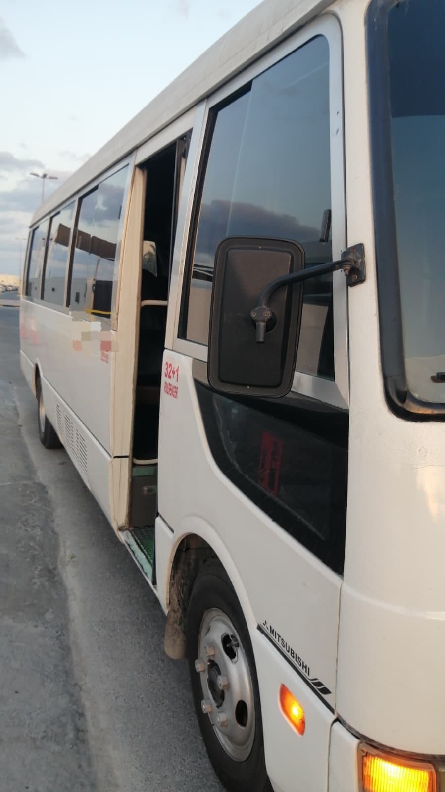 White bus with open door, parked on pavement. Black side mirror and tinted windows.