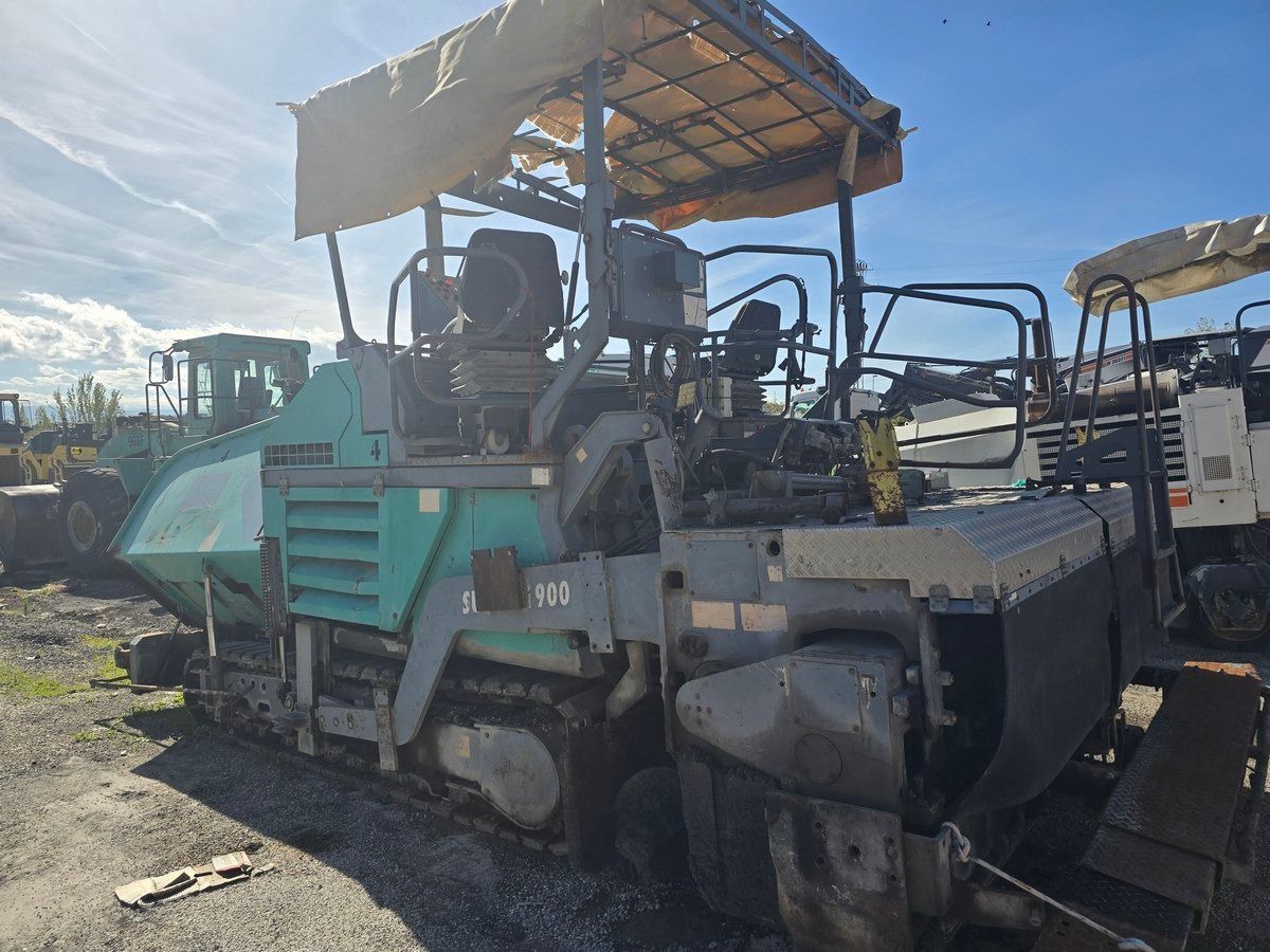 Asphalt paver machine with canopy, tracks, and control panel outdoors.