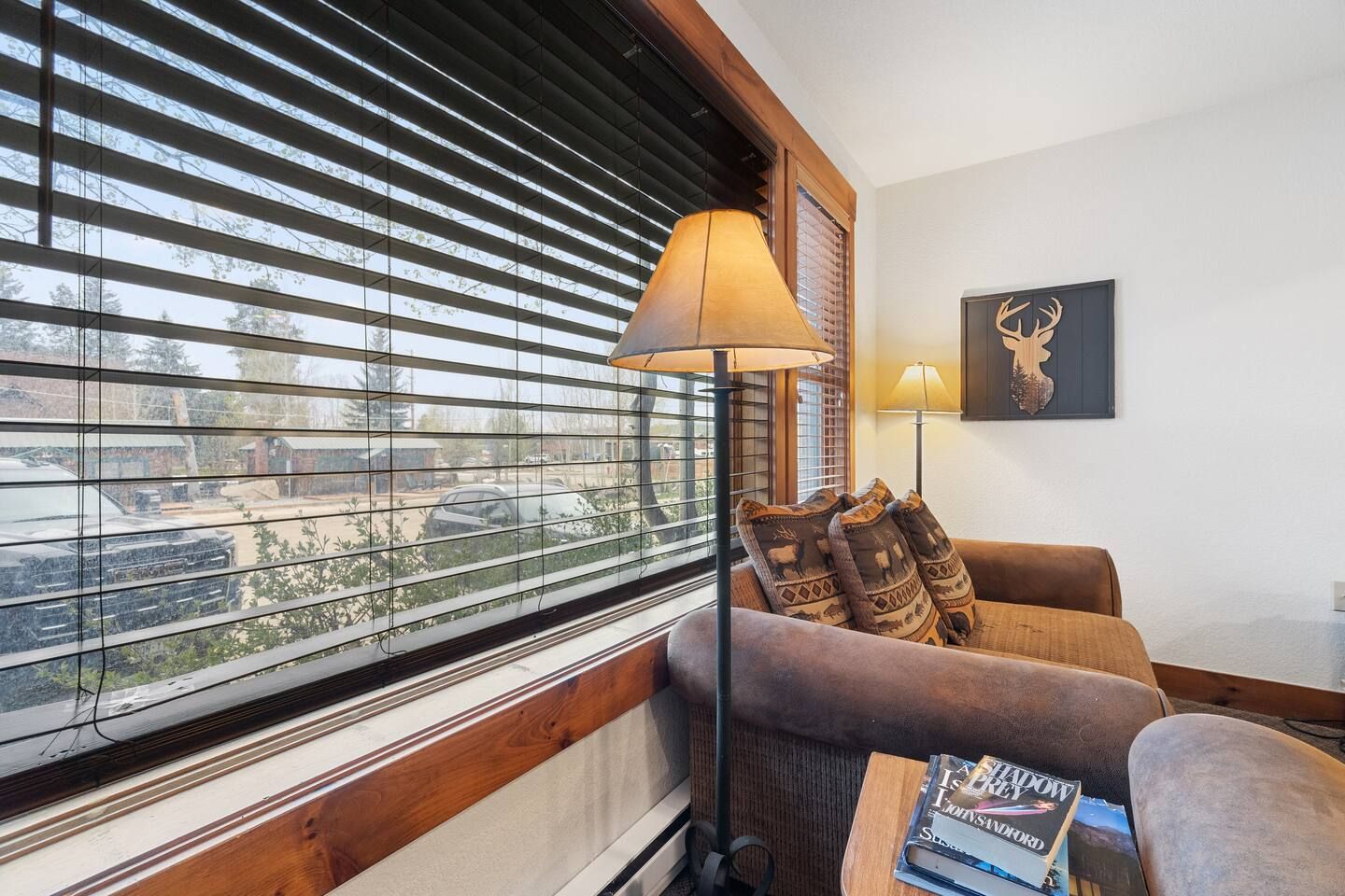 Cozy living area with a brown sofa, a floor lamp, and a large window with blinds.