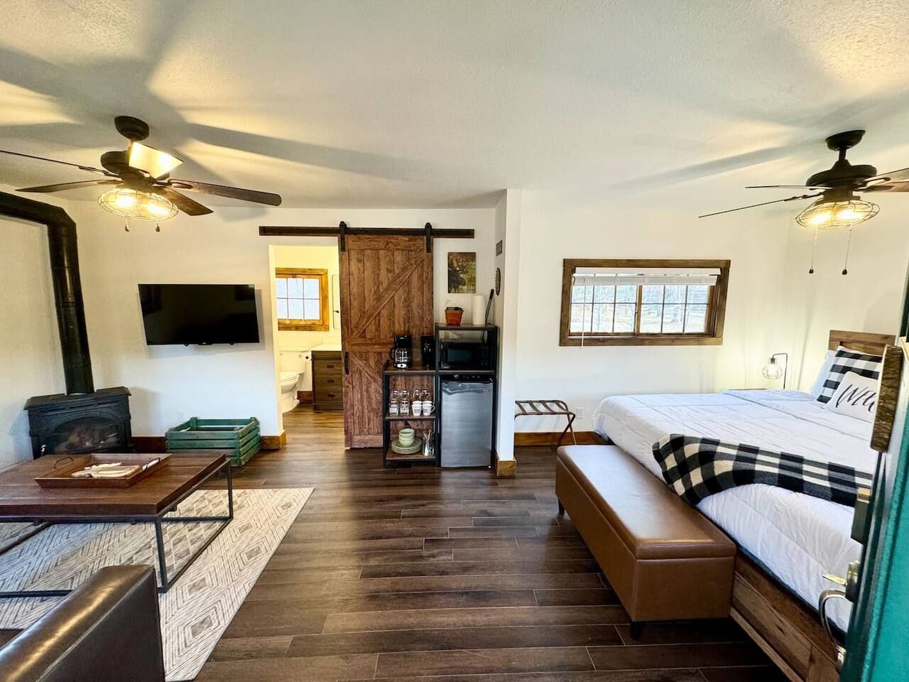 Cozy studio apartment with fireplace, TV, bed, and kitchenette. Dark wood floors and a sliding barn door.