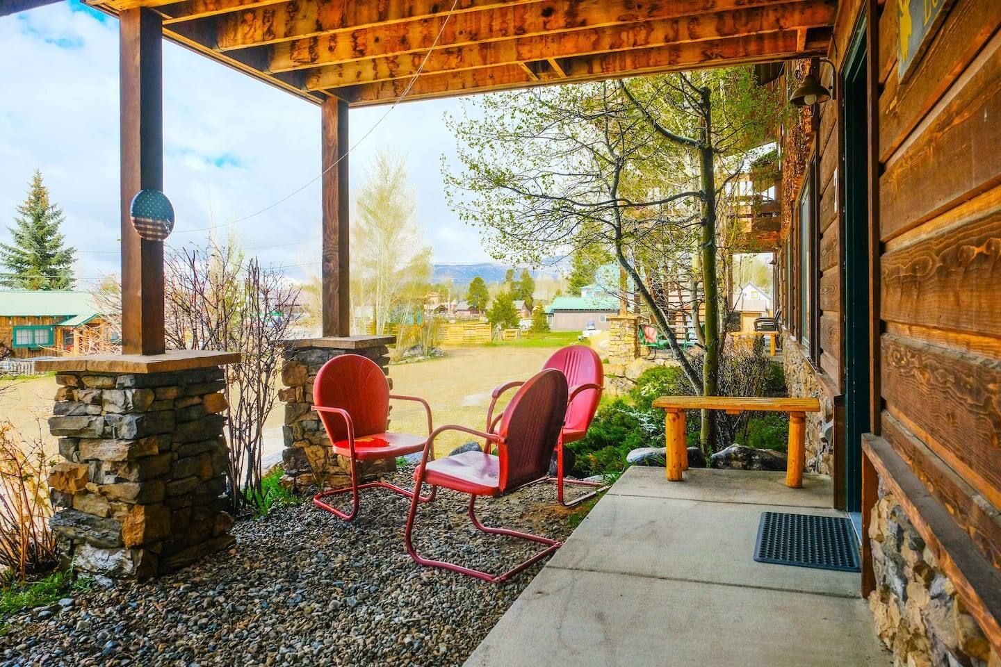 Porch with red chairs, stone pillar, and wooden ceiling. Lawn and trees in background.