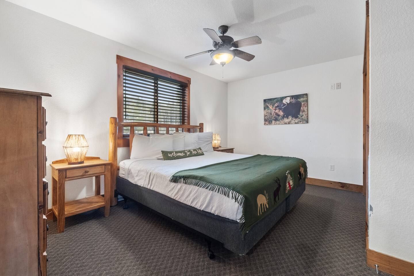 Bedroom with queen bed, nightstands, wooden furniture, and window with blinds.