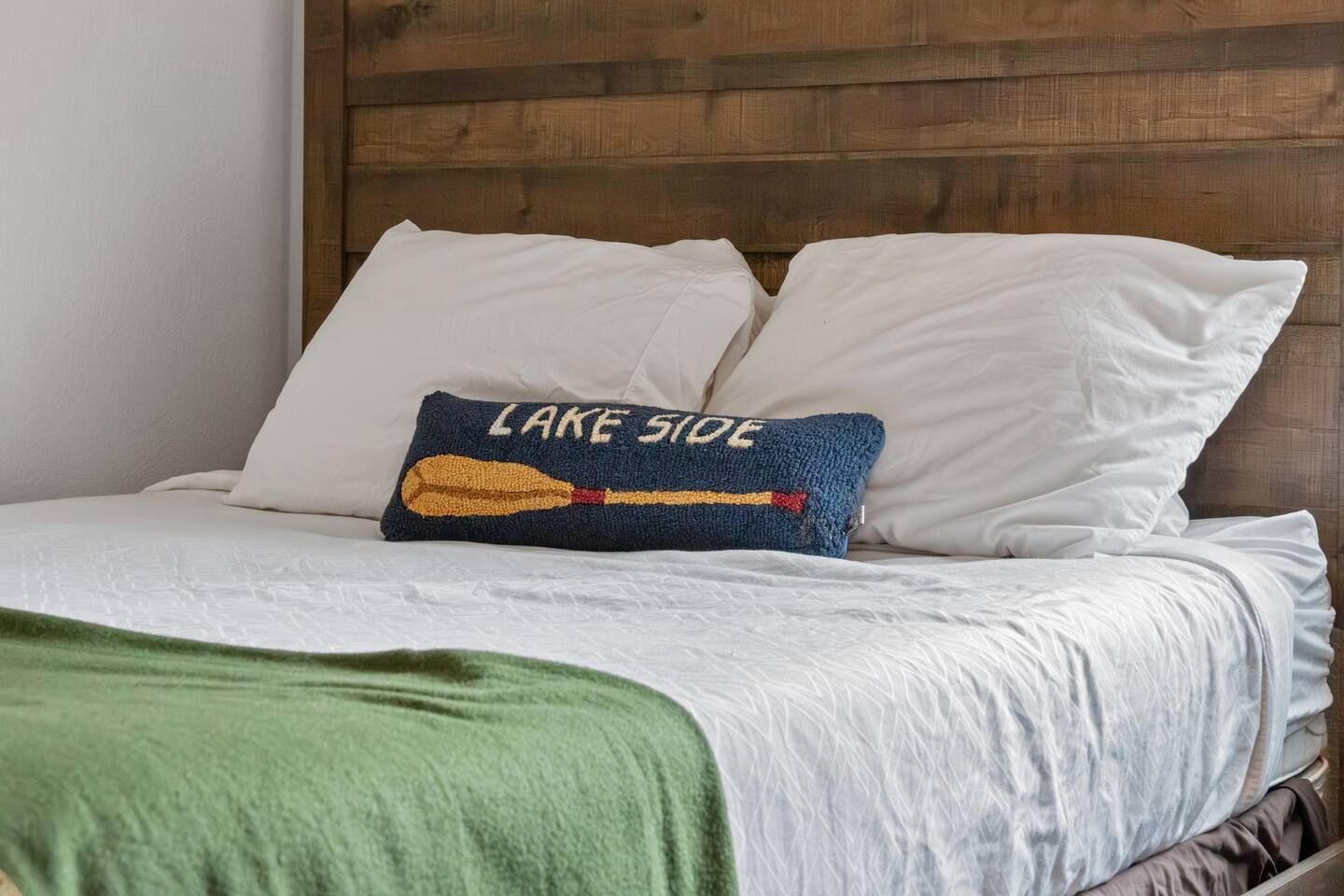 Bed with white linens, wooden headboard, green blanket, and "Lake Side" pillow.
