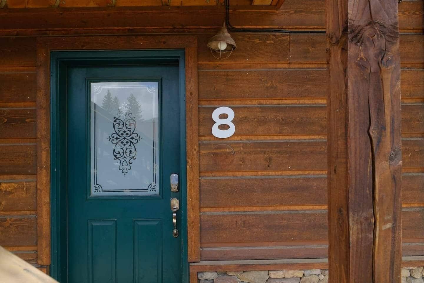 Green door with frosted glass and the number "8" on a brown wooden cabin wall.