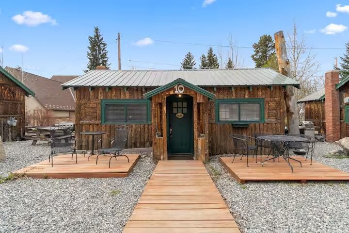 Cabin with wooden exterior, front entrance, wooden walkway, and small outdoor seating areas.