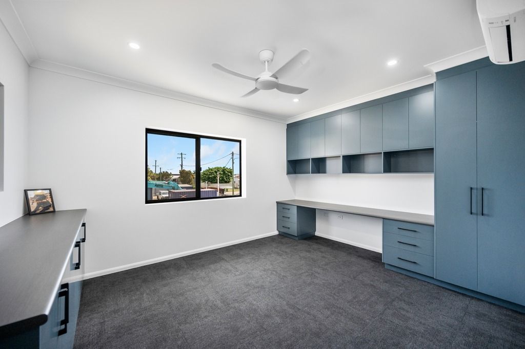 A modern room with blue built-in cabinetry, a large window, gray carpet, and a ceiling fan — Construction Company in Townsville, QLD