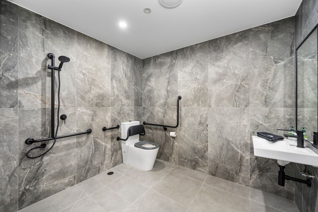 Accessible bathroom with gray tile walls and fixtures. Includes shower, toilet with grab bars, and sink — Construction Company in Townsville, QLD