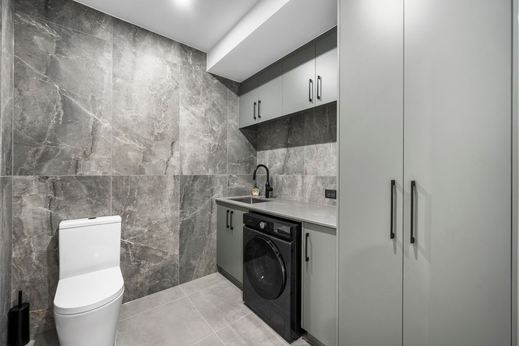 Gray laundry room with toilet, washer, sink, cabinets, and marble tile — Construction Company in Townsville, QLD