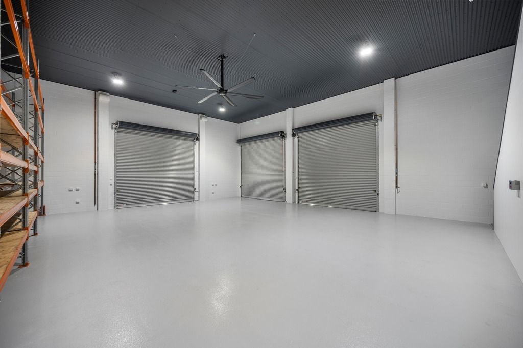 Empty warehouse interior with roller doors, white walls and floor, dark patterned ceiling, and shelving — Construction Company in Townsville, QLD