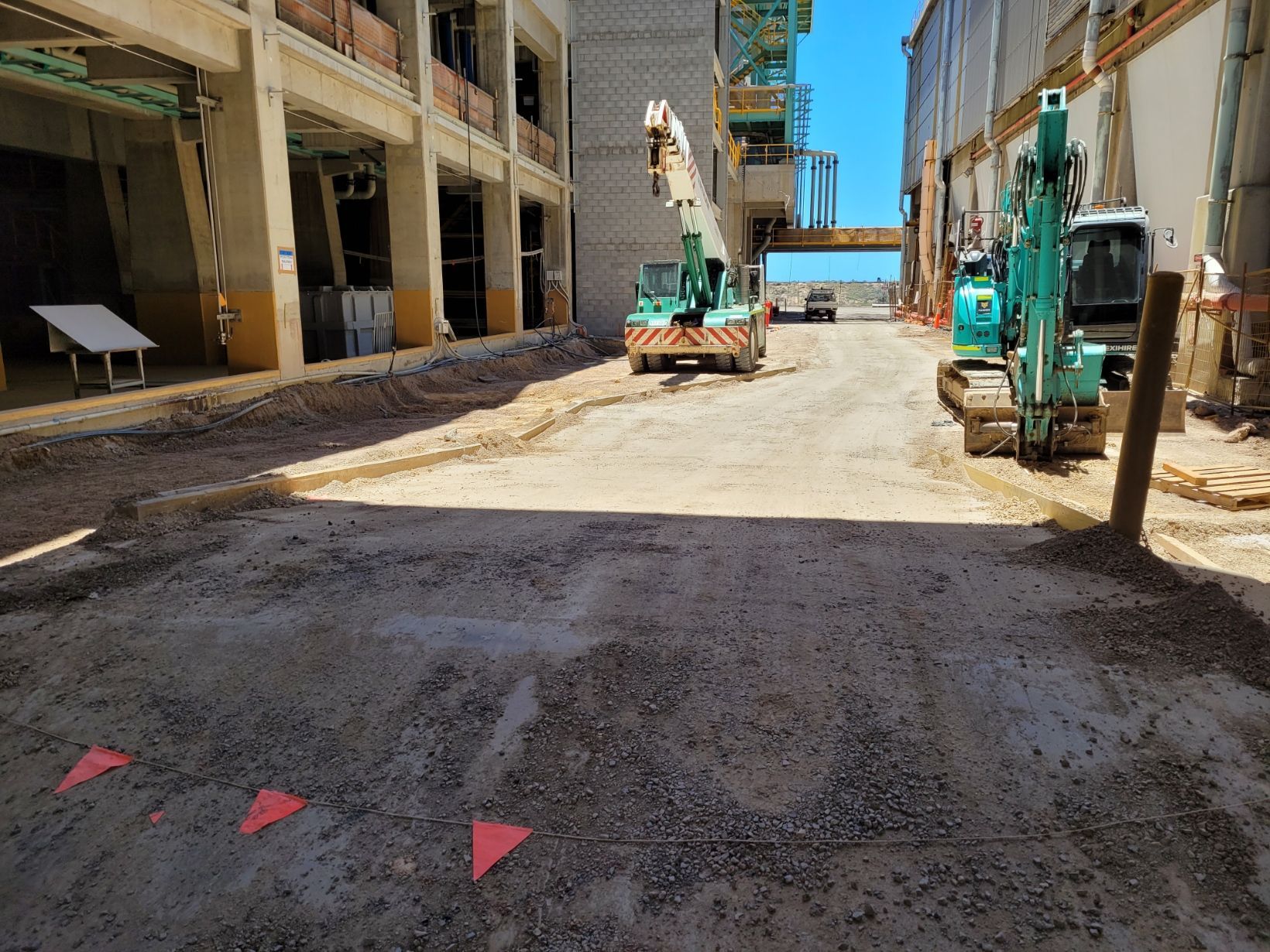 Construction site with gravel path, buildings, crane, and excavator; sunny day — Construction Company in Townsville, QLD