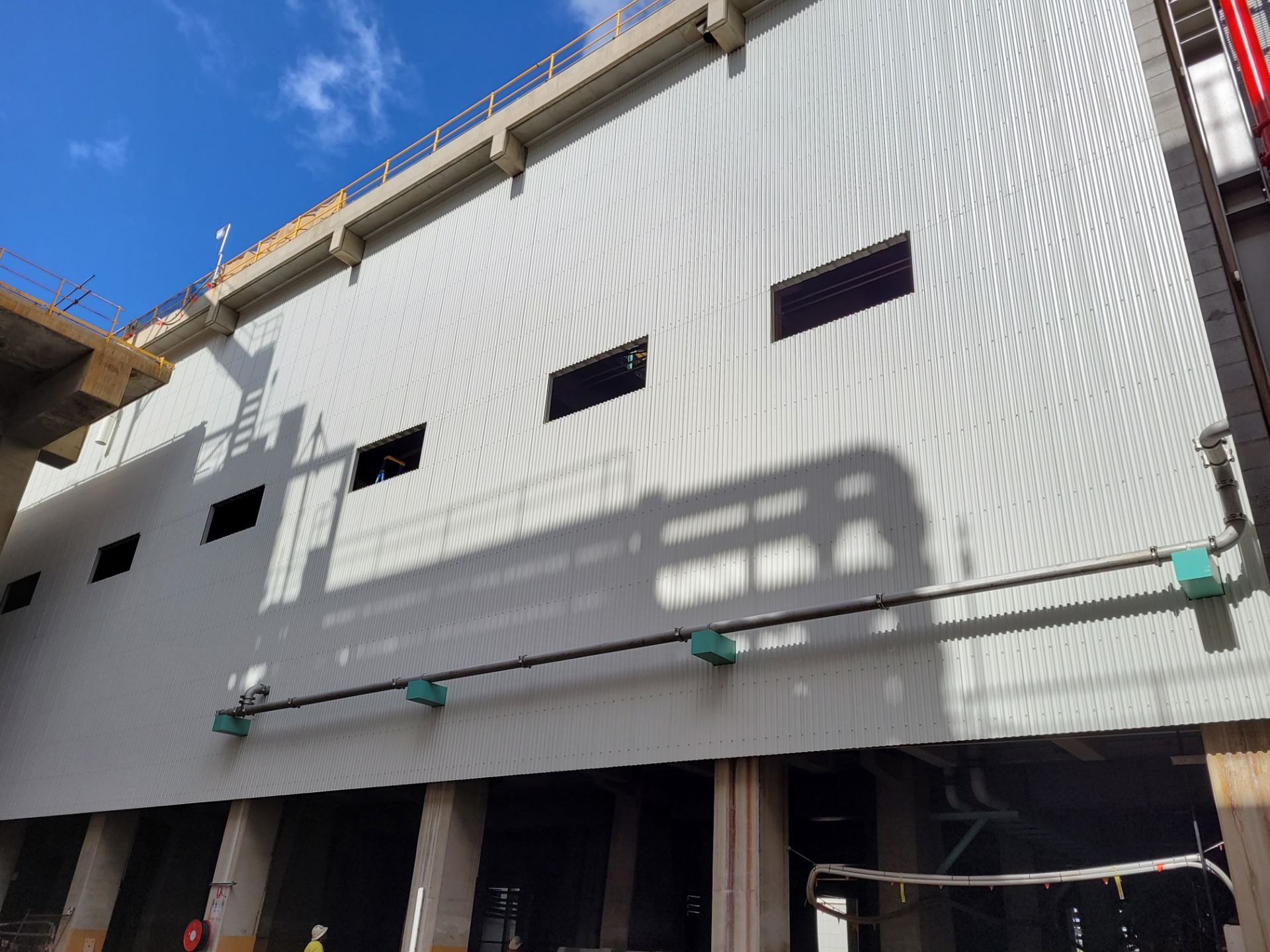Exterior of a building with a white metal facade, small windows, and exposed support beams, under a blue sky — Construction Company in Townsville, QLD