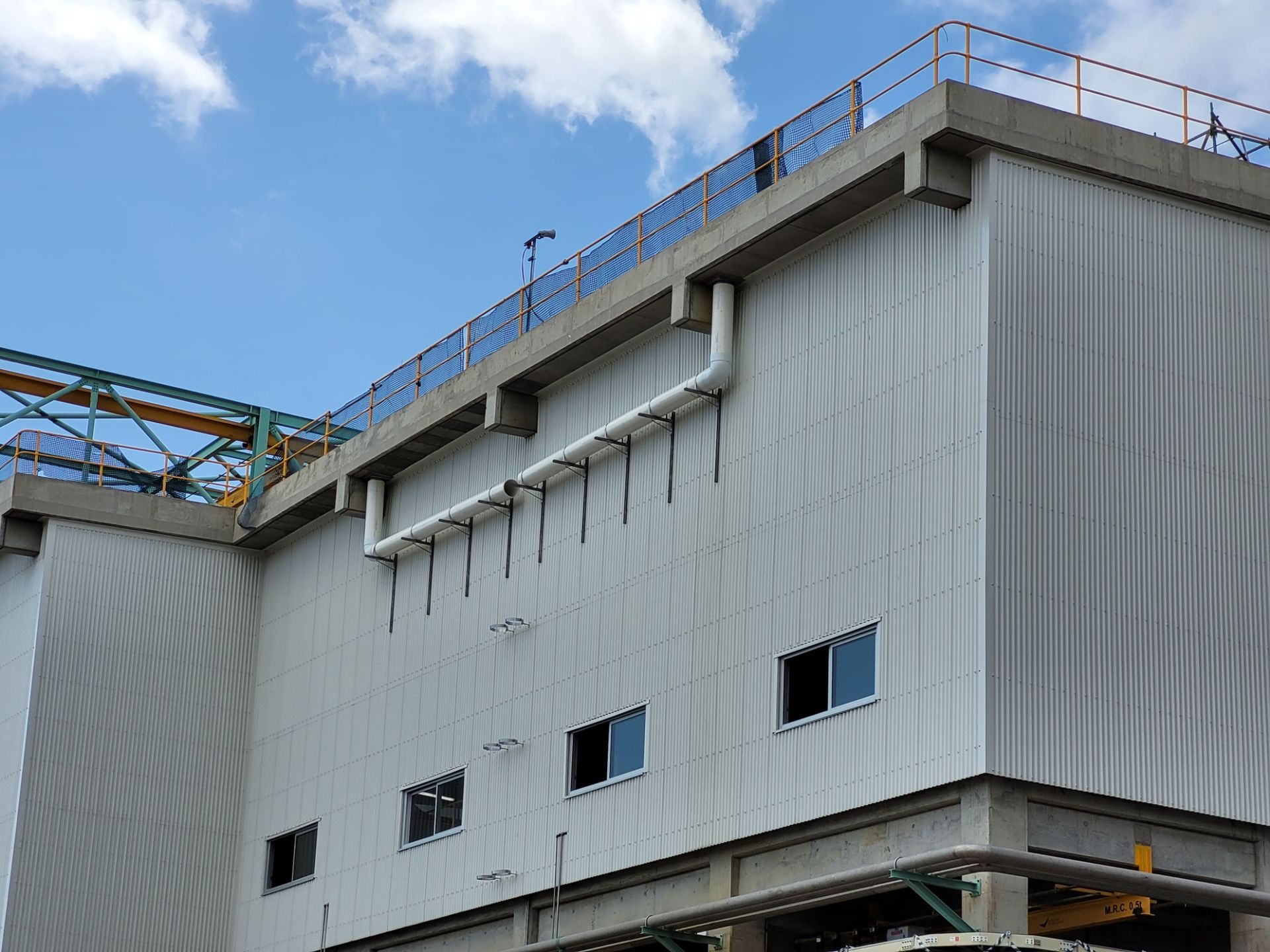 Industrial building with white corrugated metal siding, drain pipes, and small windows against a blue sky — Construction Company in Townsville, QLD