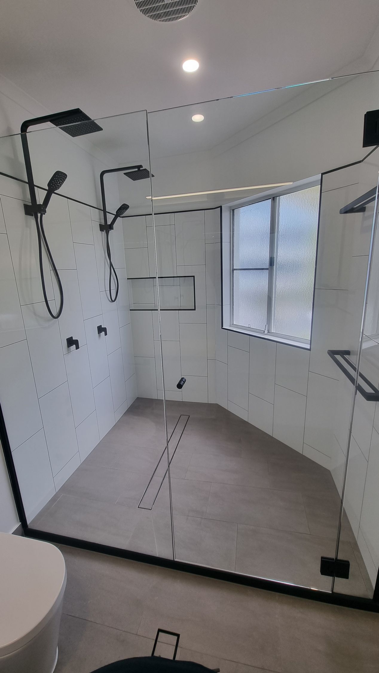 Modern shower with black fixtures, glass enclosure, white tile walls, and a gray floor — Construction Company in Townsville, QLD