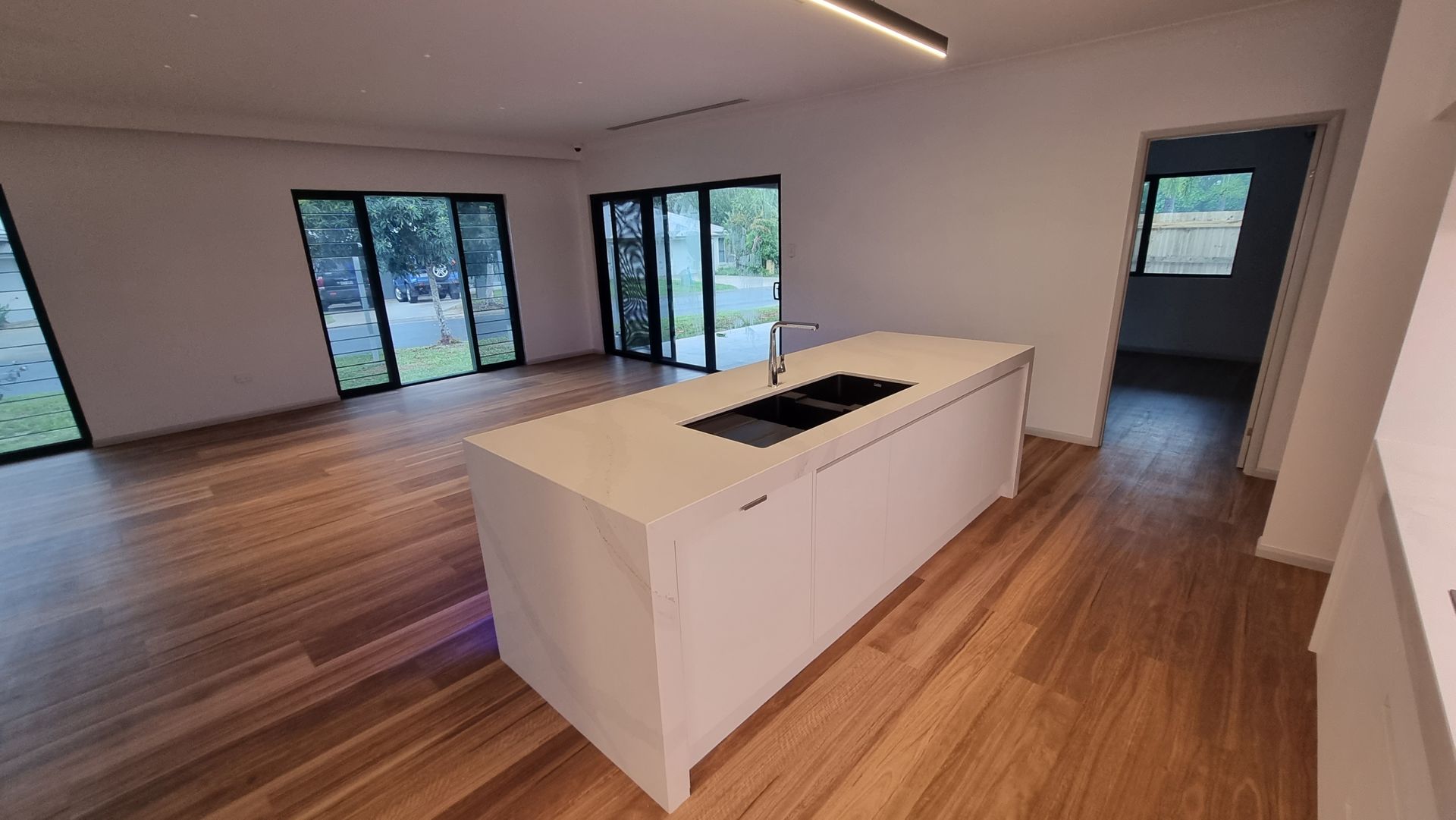 Modern kitchen with white island, wooden floors, and large glass doors — Construction Company in Townsville, QLD