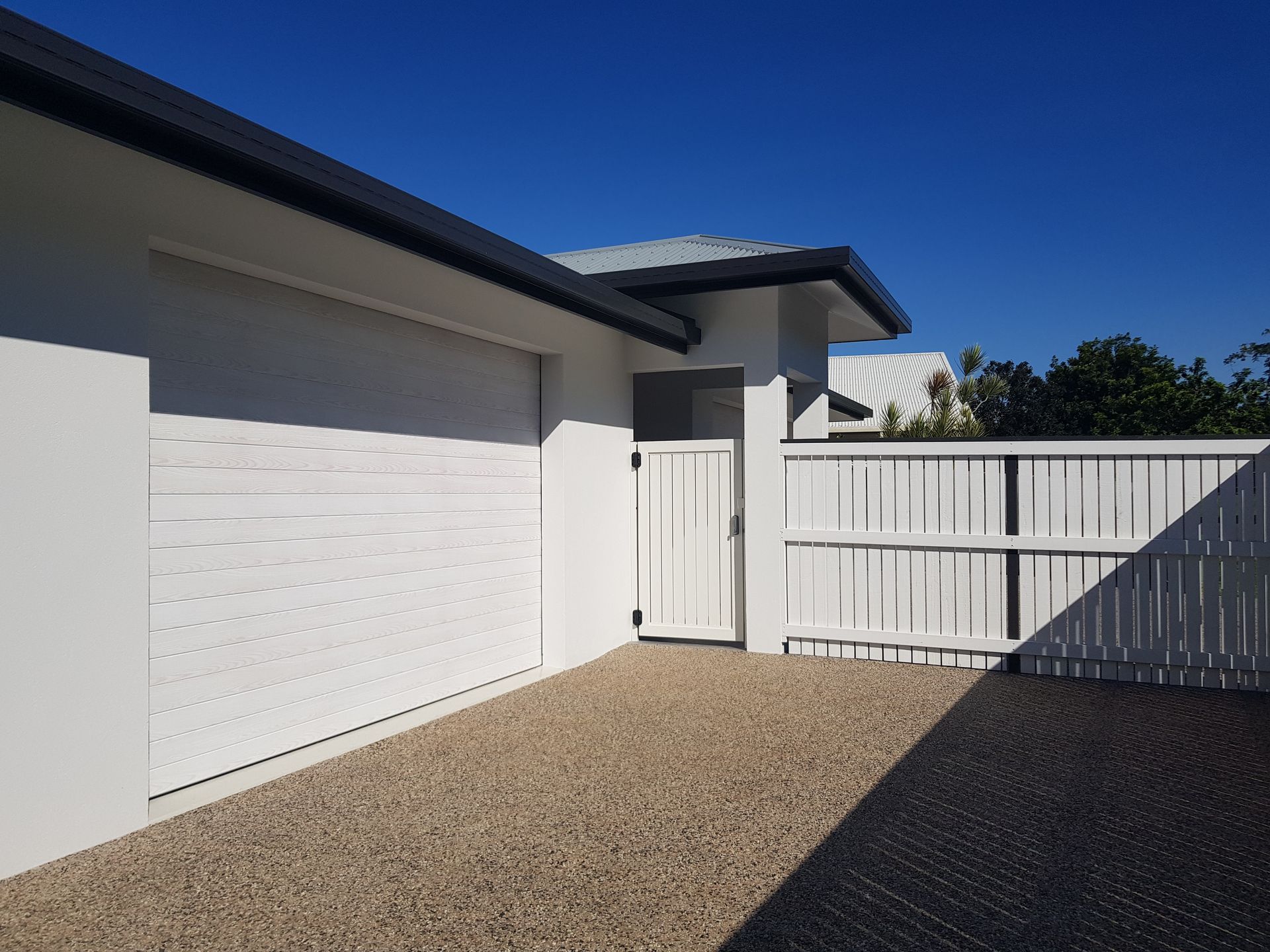 White house exterior with gravel driveway, white fence, and blue sky — Construction Company in Townsville, QLD