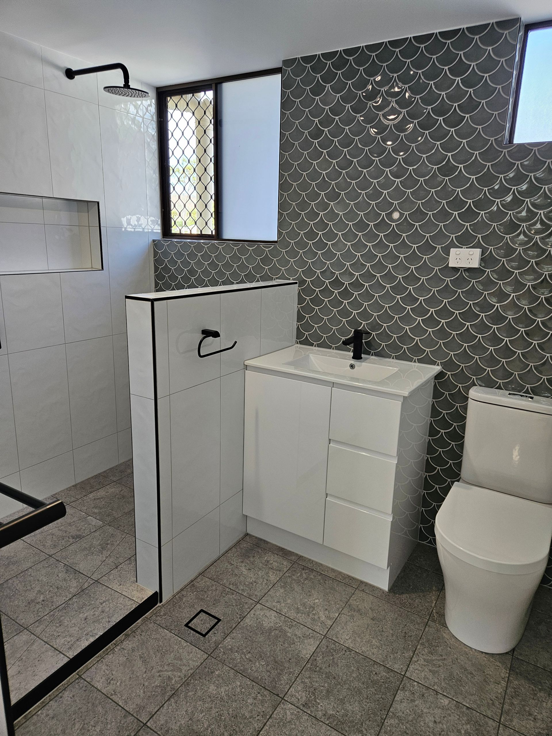 Modern bathroom with white and gray tiles, shower, vanity, toilet, and window — Construction Company in Townsville, QLD