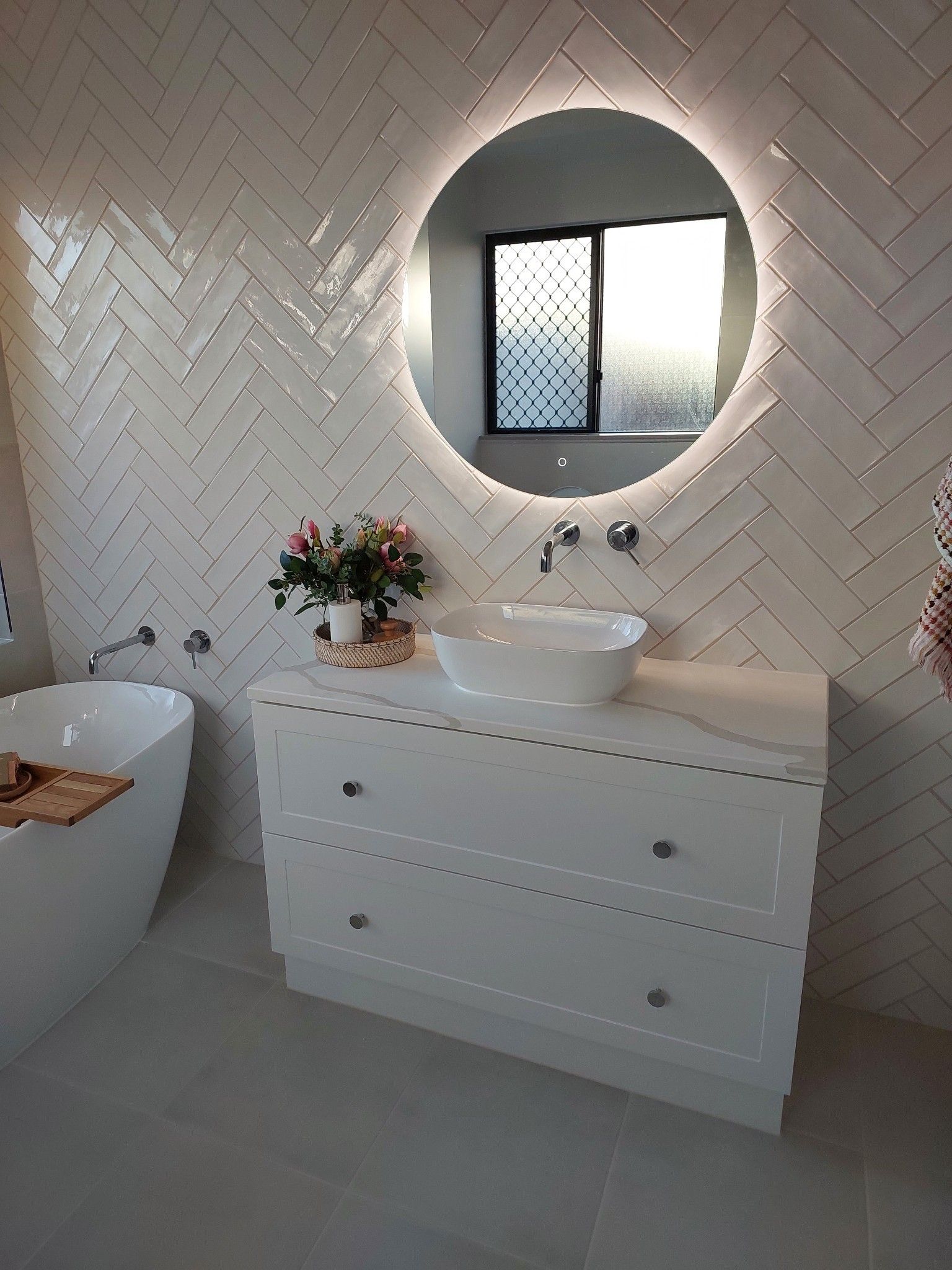 Modern bathroom with a white vanity, round mirror, herringbone tile, and a freestanding tub — Construction Company in Townsville, QLD