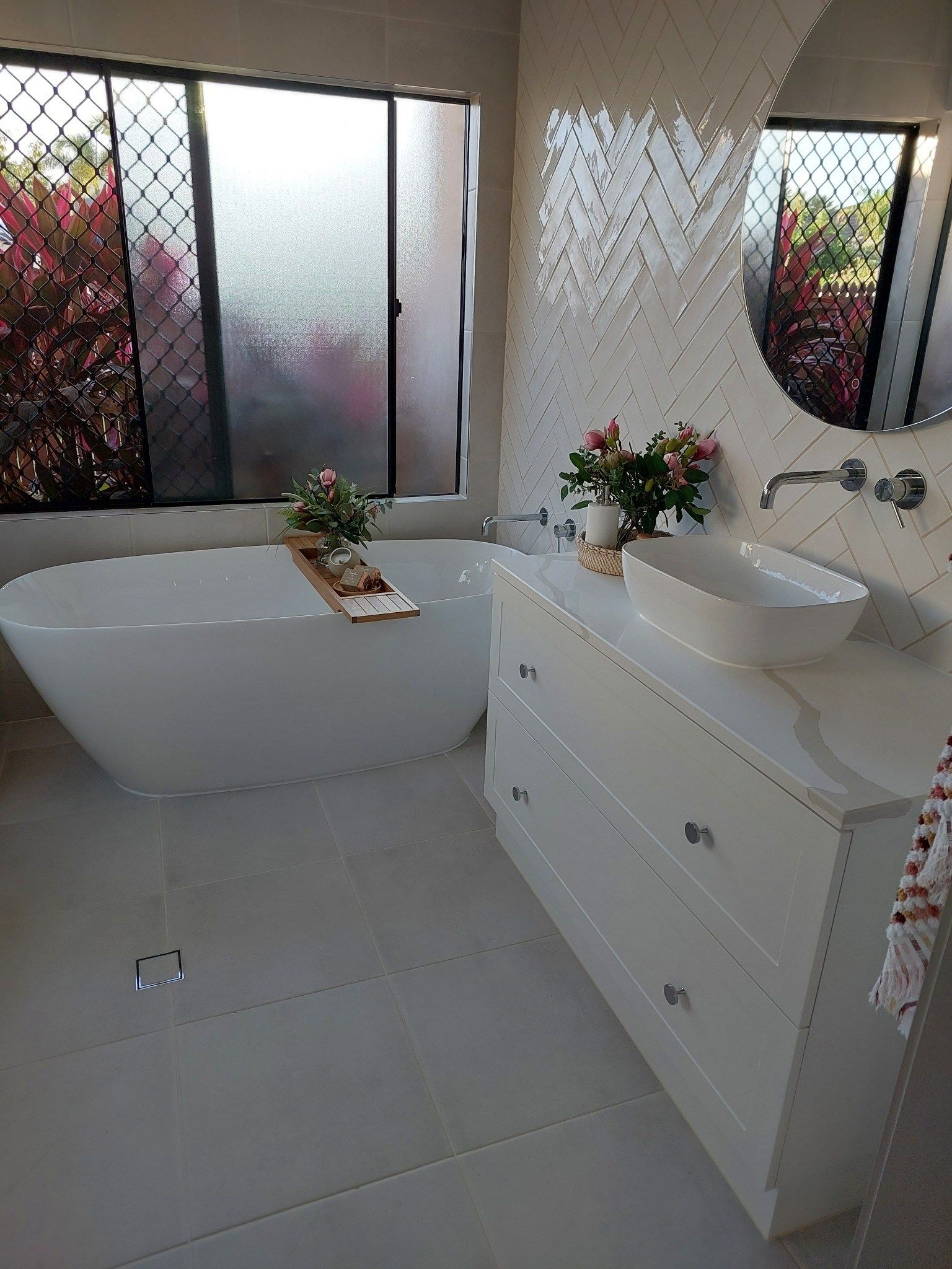 White bathroom with a bathtub, vanity, and window overlooking a garden — Construction Company in Townsville, QLD