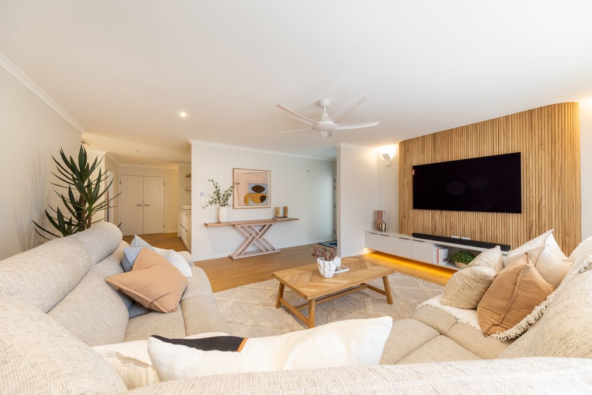 Cozy living room with large white sofa, wooden accent wall with TV, and natural light. — Construction Company in Townsville, QLD