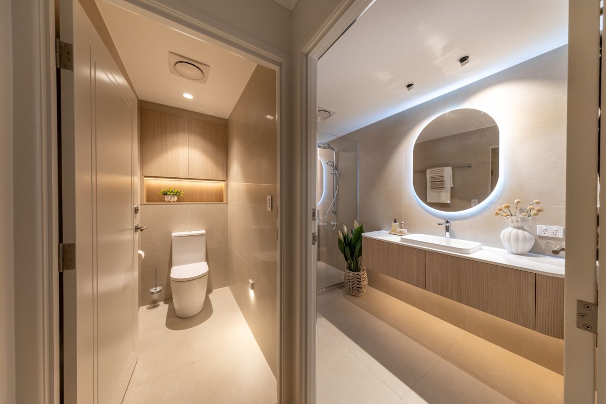 Hallway view into two bathrooms: one with toilet, the other with vanity and mirror. Light wood cabinets and walls. — Construction Company in Townsville, QLD
