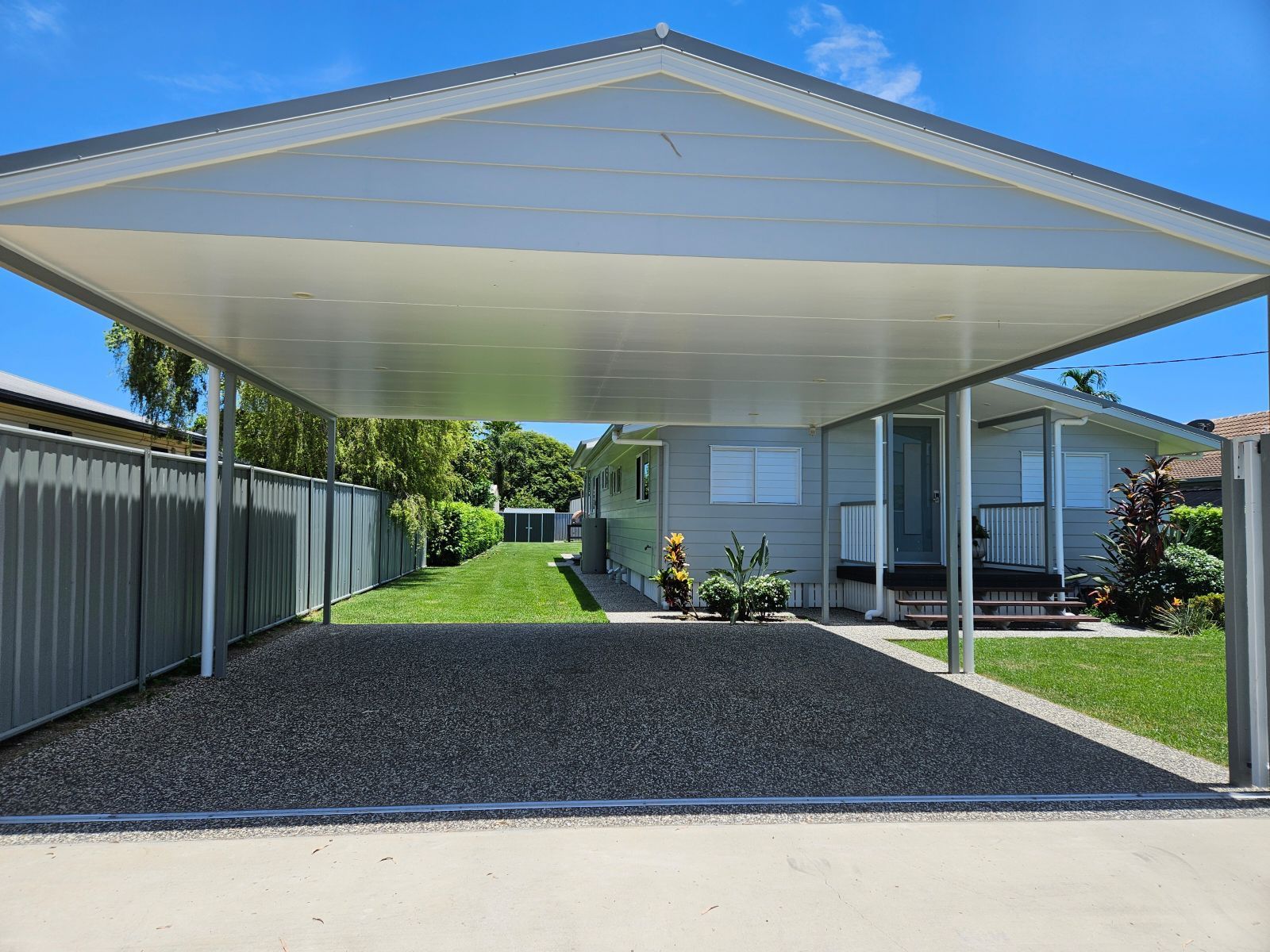 Carport covering a gravel driveway in front of a house, next to a gray fence and grass — Construction Company in Townsville, QLD