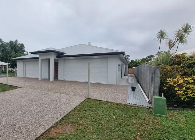 A modern, single-story house with a gravel driveway and three garage doors under a cloudy sky — Construction Company in Townsville, QLD