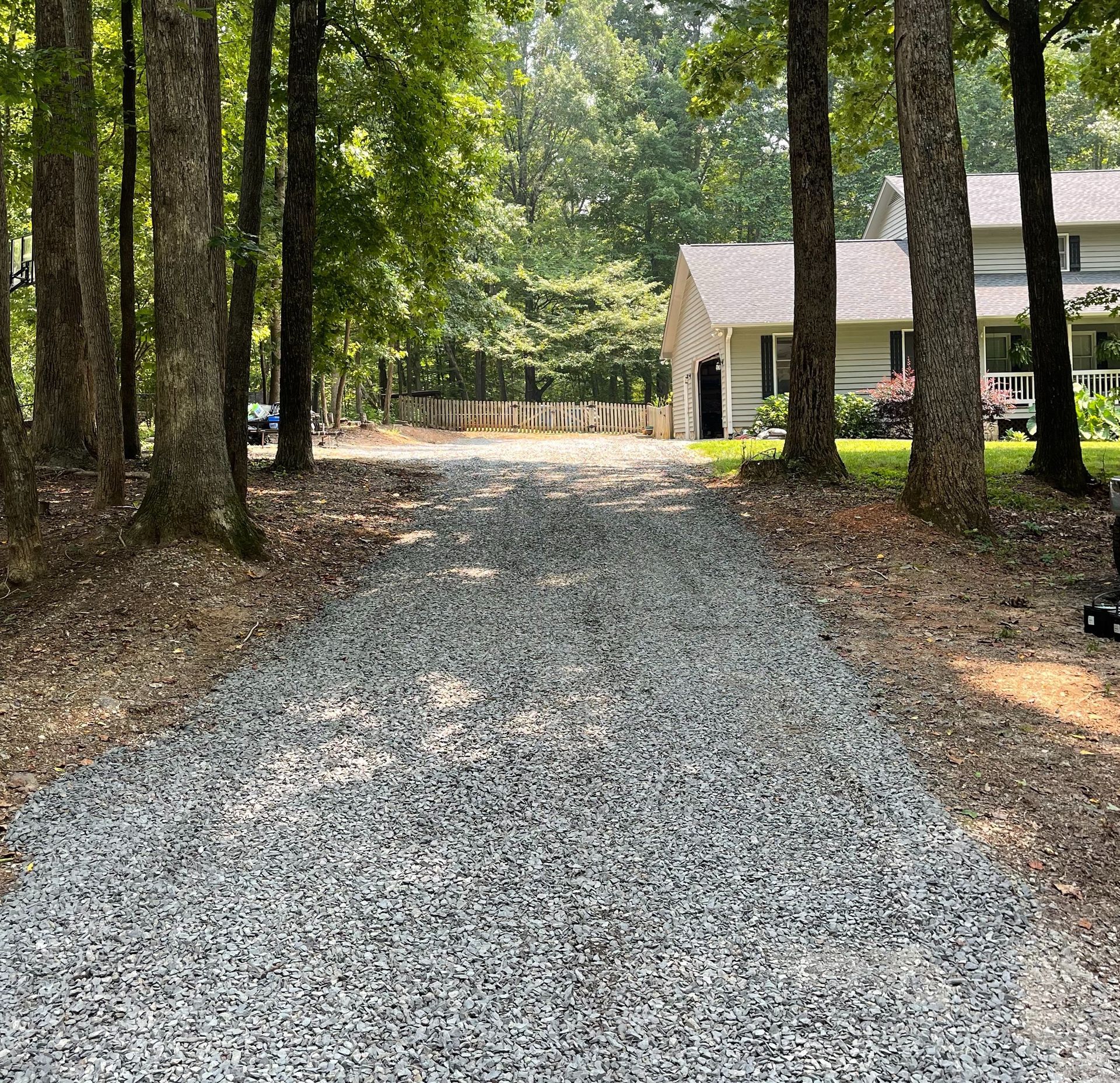 A gravel driveway leading to a house in the woods.