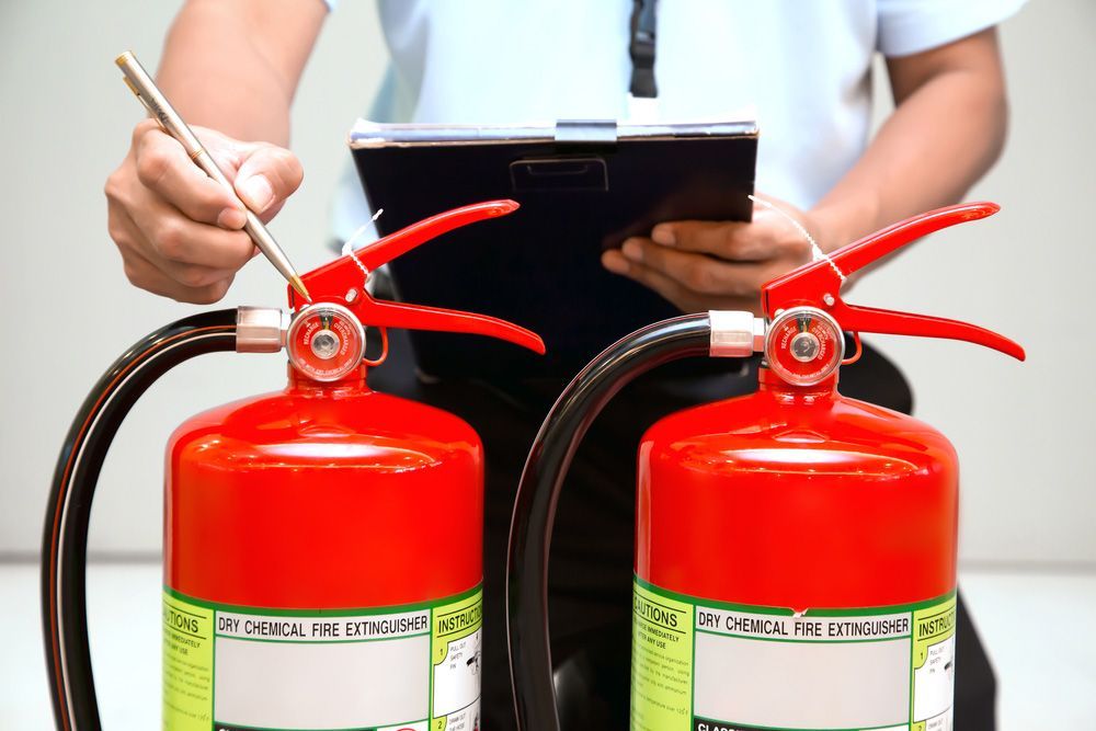 A Man Is Sitting Next to Two Fire Extinguishers and Writing on A Clipboard — Fireline 2000 Fire Equipment Pty Ltd in Brisbane, QLD