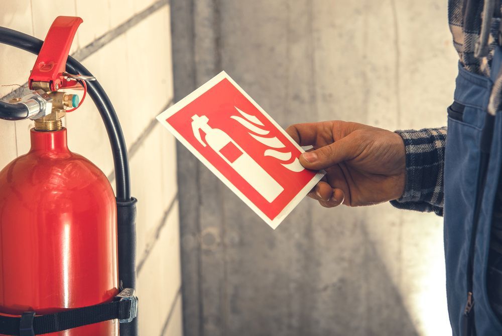 A Man Is Holding a Fire Extinguisher Sign in Front of A Fire Extinguisher — — Fireline 2000 Fire Equipment Pty Ltd in Brisbane, QLD