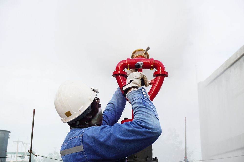 A Man in A Hard Hat Is Working on A Red Hydrant — Fireline 2000 Fire Equipment Pty Ltd in Brisbane, QLD