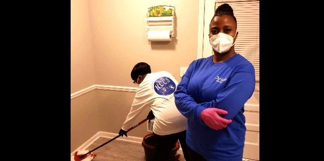 A woman wearing a mask is standing next to a man cleaning the floor.
