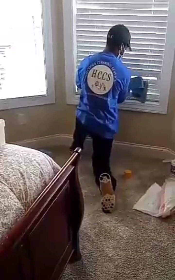 A man in a blue shirt is cleaning a window in a bedroom.
