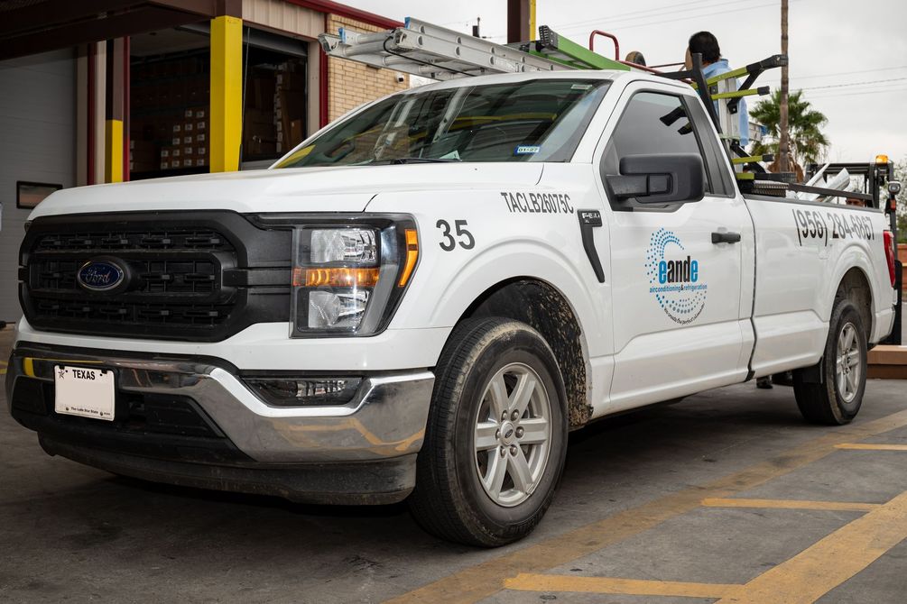 White utility pickup truck parked at a service bay, with tools and equipment in the bed