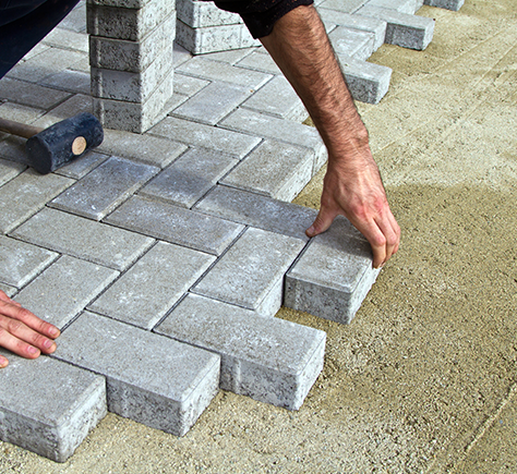 a man is laying bricks on the ground with a hammer .