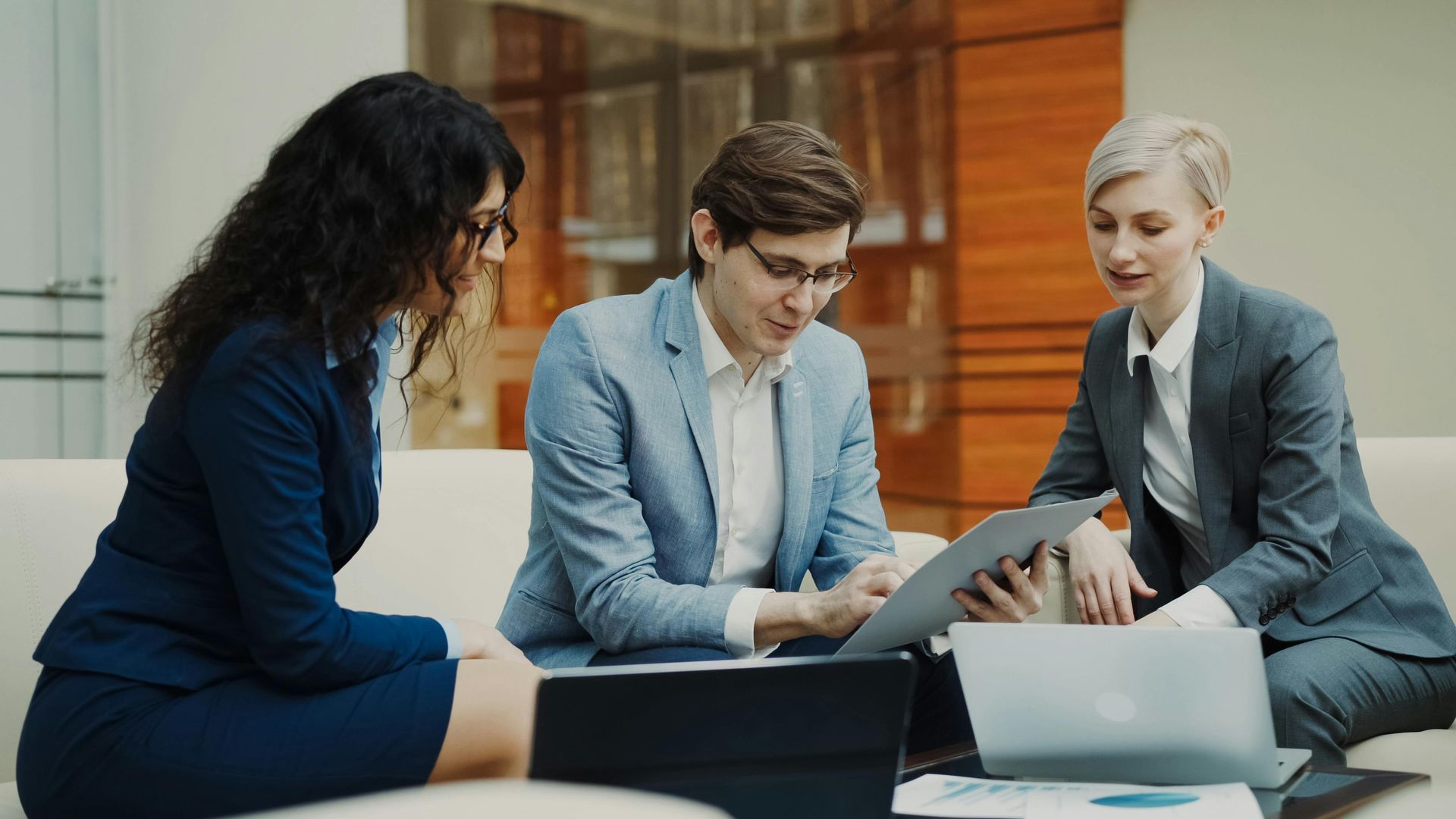 Three colleagues in professional attire collaborate while reviewing documents and a laptop in a brightly lit office.