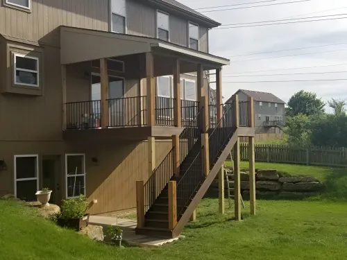 A two-story house with a wooden deck and stairs leading down to a grassy yard.