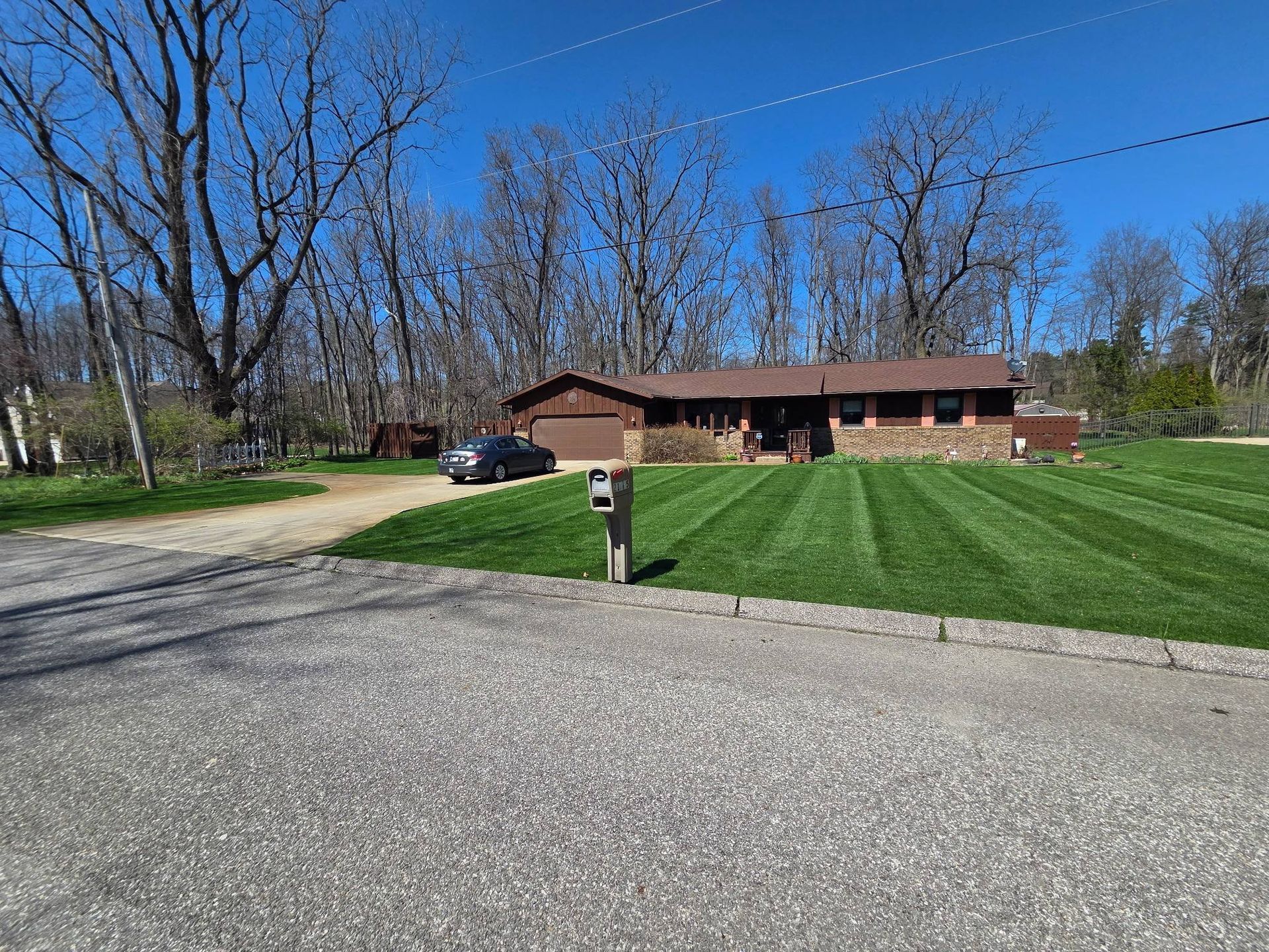 Suburban house with a manicured lawn, driveway, and parked car under a clear blue sky